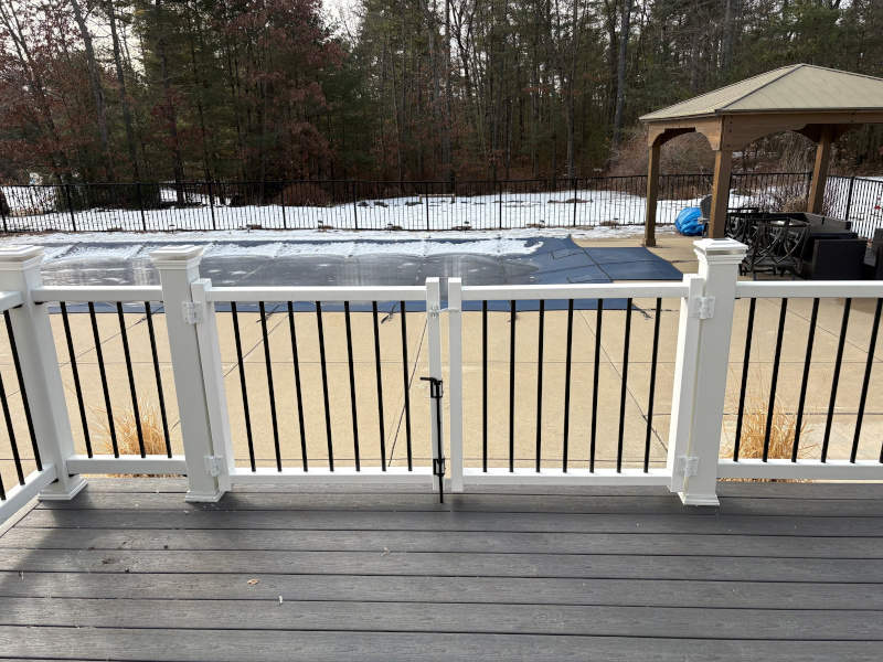 This Litchfield, NH project features a clean, modern custom deck fencing installation by Granite State Fence, designed for both safety and style. The focal point of the project is a 6-foot-high custom composite double drive gate with a 78-inch opening, combining white composite posts and rails with black vertical balusters. The contrast creates a sharp, timeless look that complements the deck while maintaining clear sightlines to the backyard and pool area. Each post was carefully set and capped for a finished appearance, and the double gate was custom-built to provide smooth operation and durability. This setup offers secure access while still feeling open and inviting, an ideal solution for decks overlooking pools or large outdoor living spaces. From precise spacing to clean hardware placement, every detail was thoughtfully executed to ensure long-term performance and a polished final result. A great example of how custom fencing can elevate both the function and aesthetics of an outdoor space.